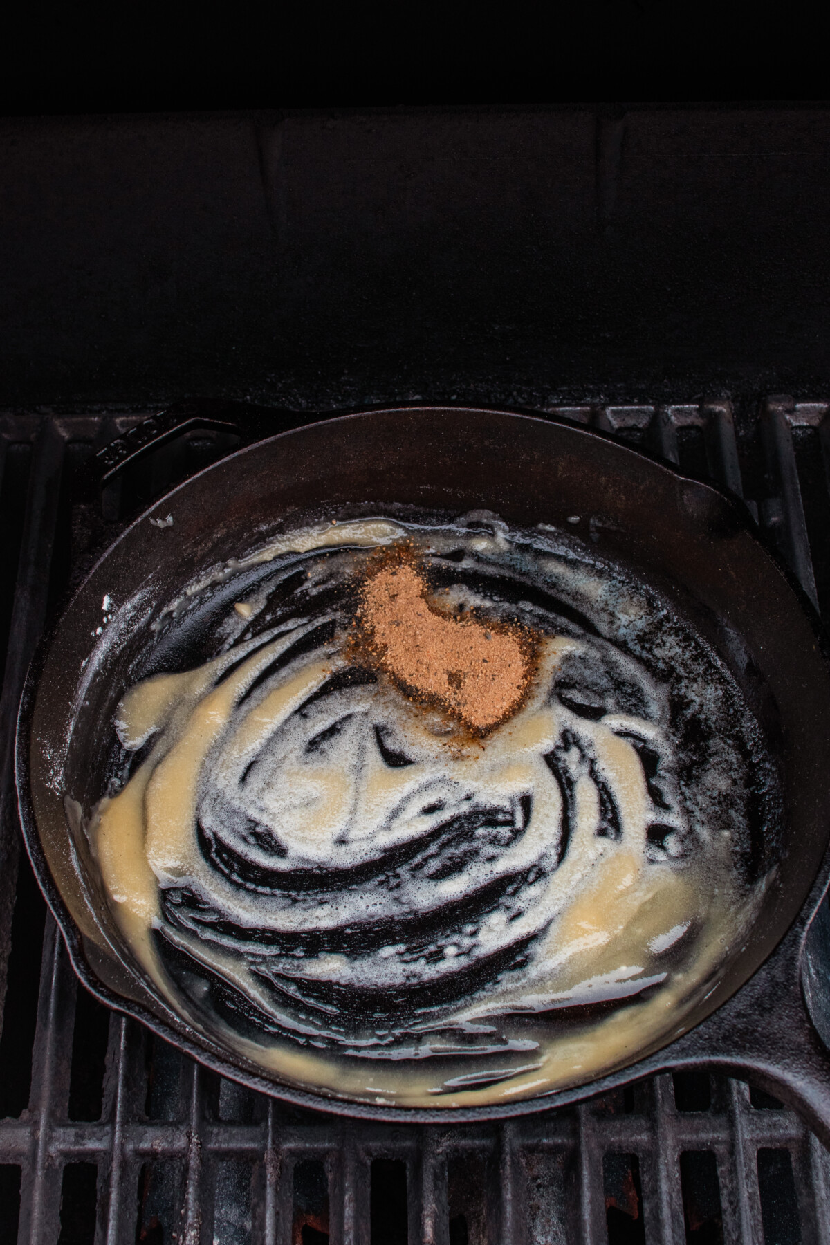 Roux being formed with butter and flour and umami powder added in cast iron skillet on grill.