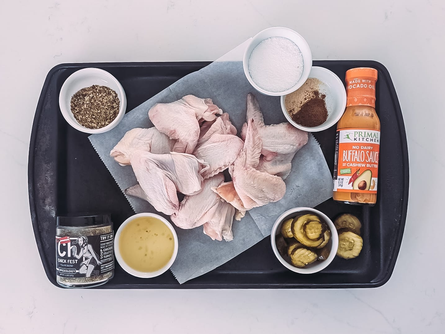 ingredients for pickle brined chicken wings showing wings, spices, pickle juice and buffalo sauce