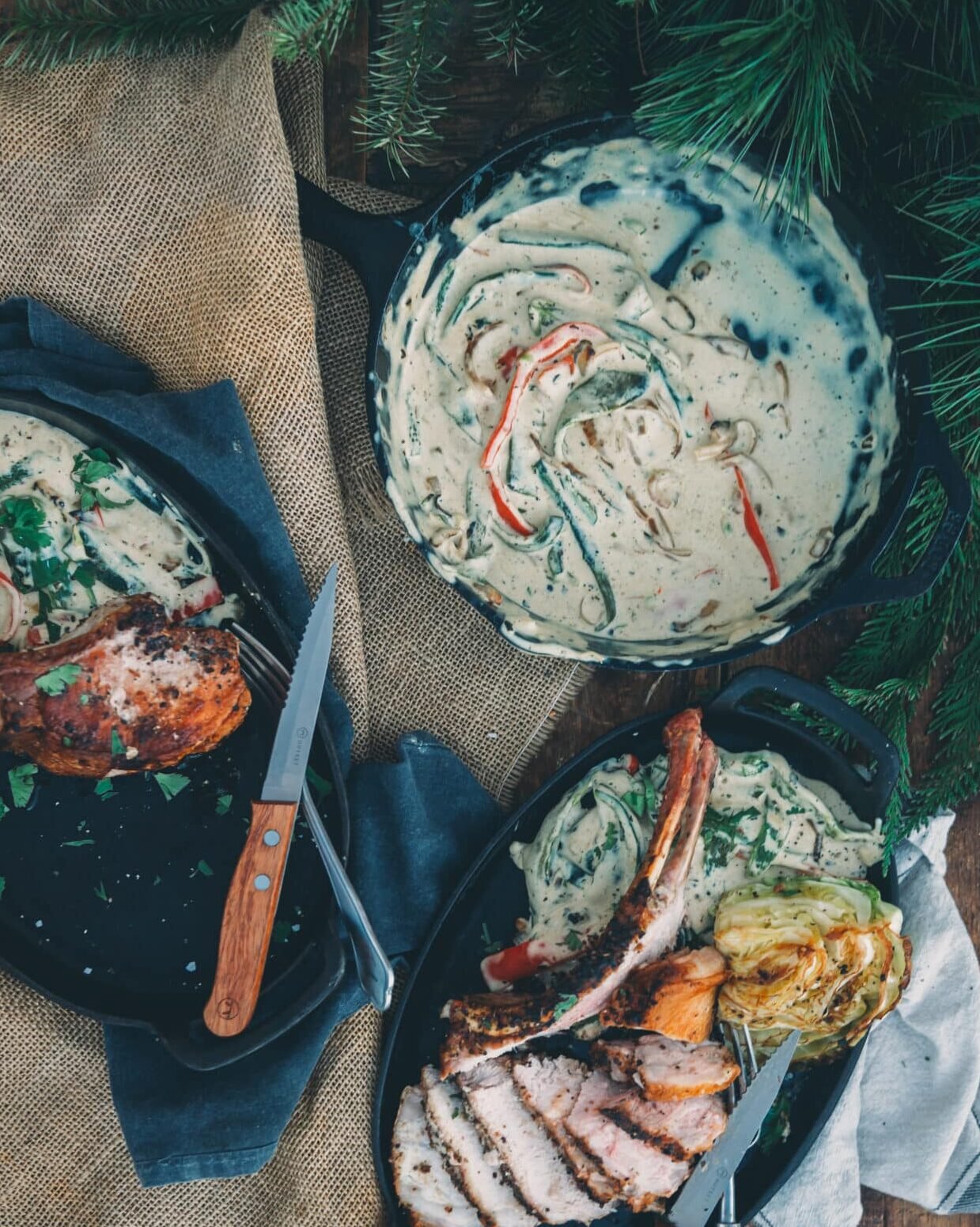 Overhead shot of skillet filled with cheesy creamy peppers in sauce on a rustic table with pork chops. 