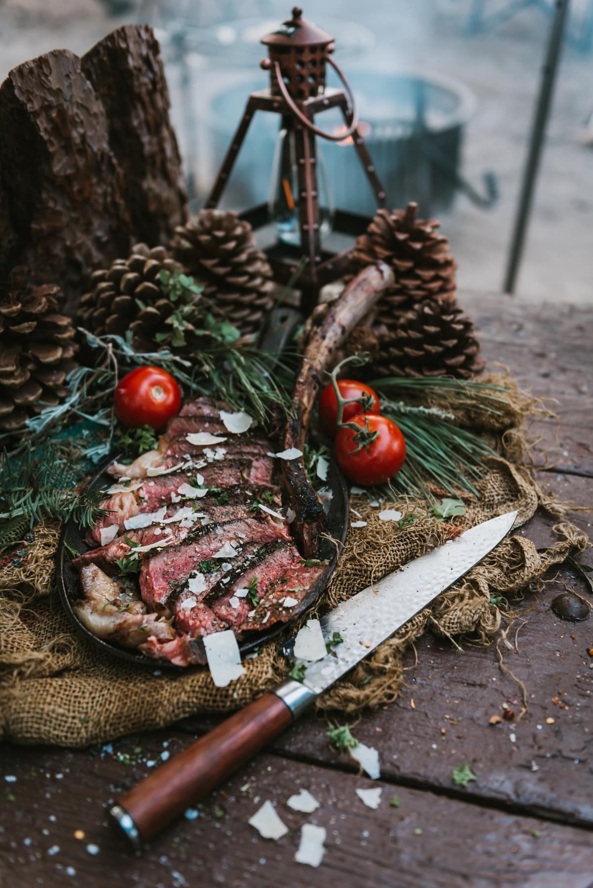 Campfire grilled tomahawk steak sliced and plated with shaved parmesan cheese and garnish on a rustic table 