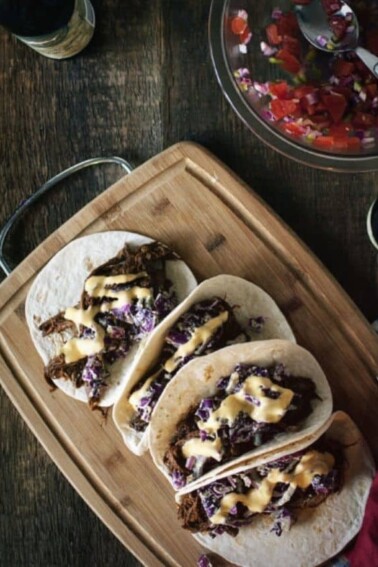 Flat lay photo of BBQ Brisket Tacos with Dubliner Cheese Sauce, served with salsa on the side on a wooden board.