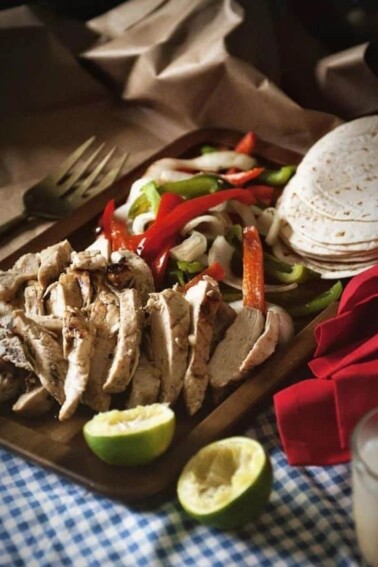 Charcoal Grilled Chicken Fajitas served on a wooden board with slices of lime.