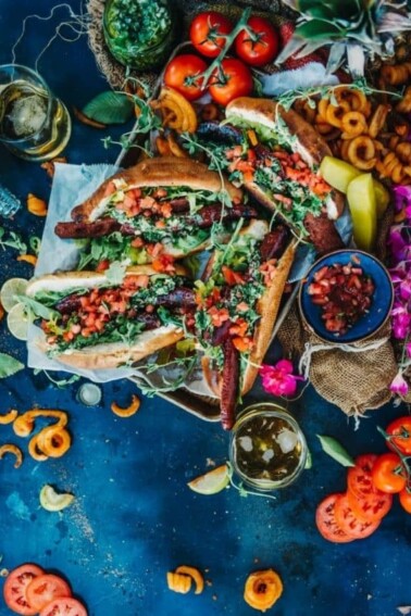 A colorful flat lay photo of Choripan: Argentinian Style Grilled Sausage Sandwiches surrounded by condiments and sides.