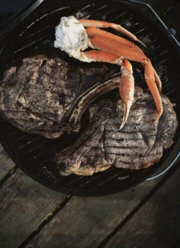 Grilled Rib Eyes & Snow Crab on a black plate.