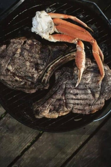 Grilled Rib Eyes & Snow Crab on a black plate.