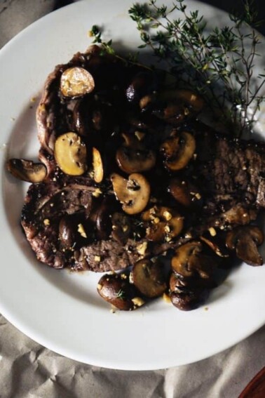 Grilled T-Bone Steaks with Thyme Mushrooms served on a white plate.