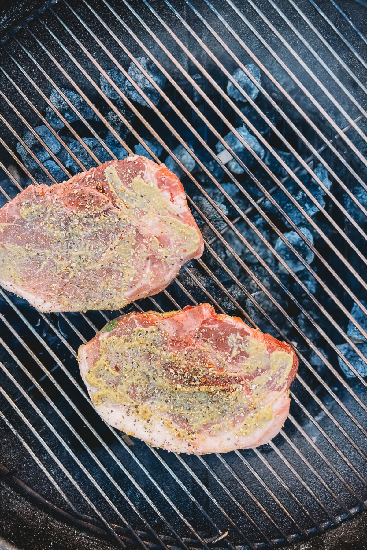 2 pork chops rubbed with mustard and spices on a grill.
