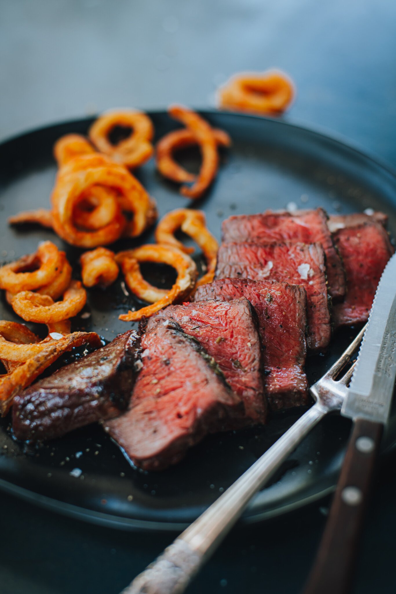 Close up of sliced petit top sirloin steak, cooked to a pink medium rare center, seasoned with salt and fries in the background.