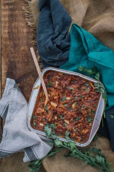 A tray of Slow Smoked Pork and Beans with a wooden spoon sticking on top of it, while placed on a wooden surface.