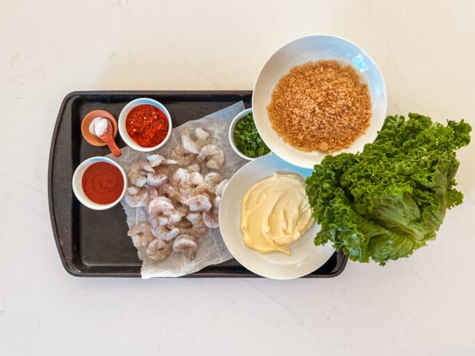 What you need for keto bang bang shrimo with ingredients arranged; shrimp, mayo, sriracha, pork panko and more in bowls on a tray. 