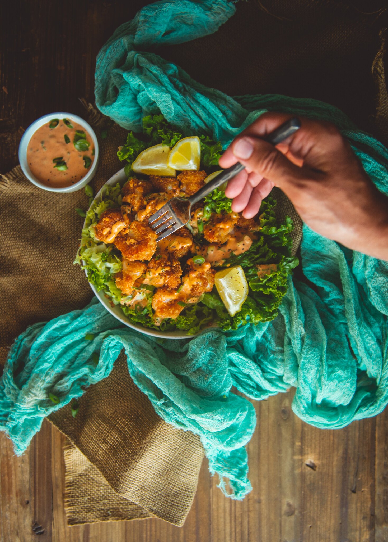 Hand with fork picking up crispy bang bang shrimp over bowl of more air fried shrimps and lettuce. 