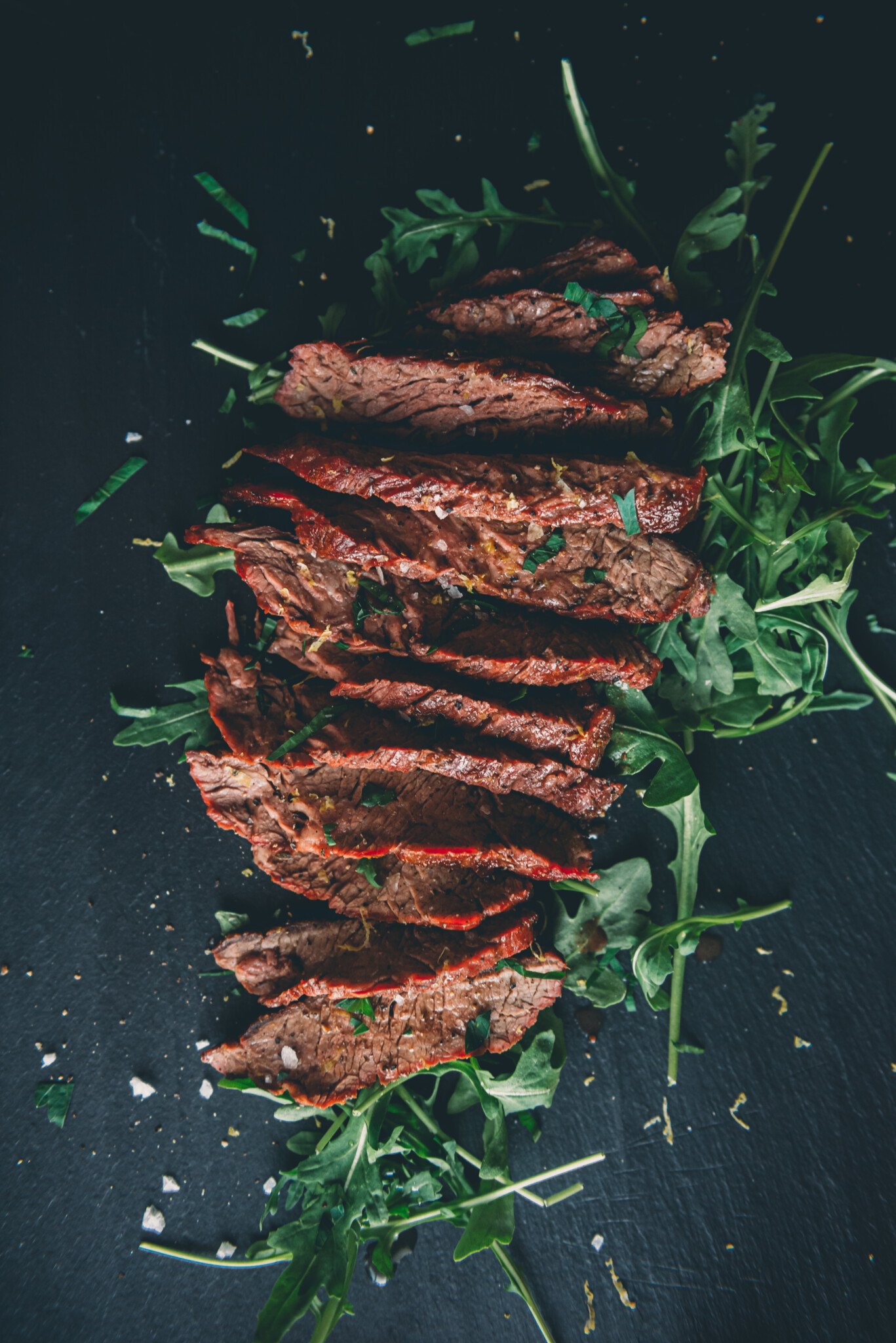 Sliced bavette steak over arugula on black slate. 