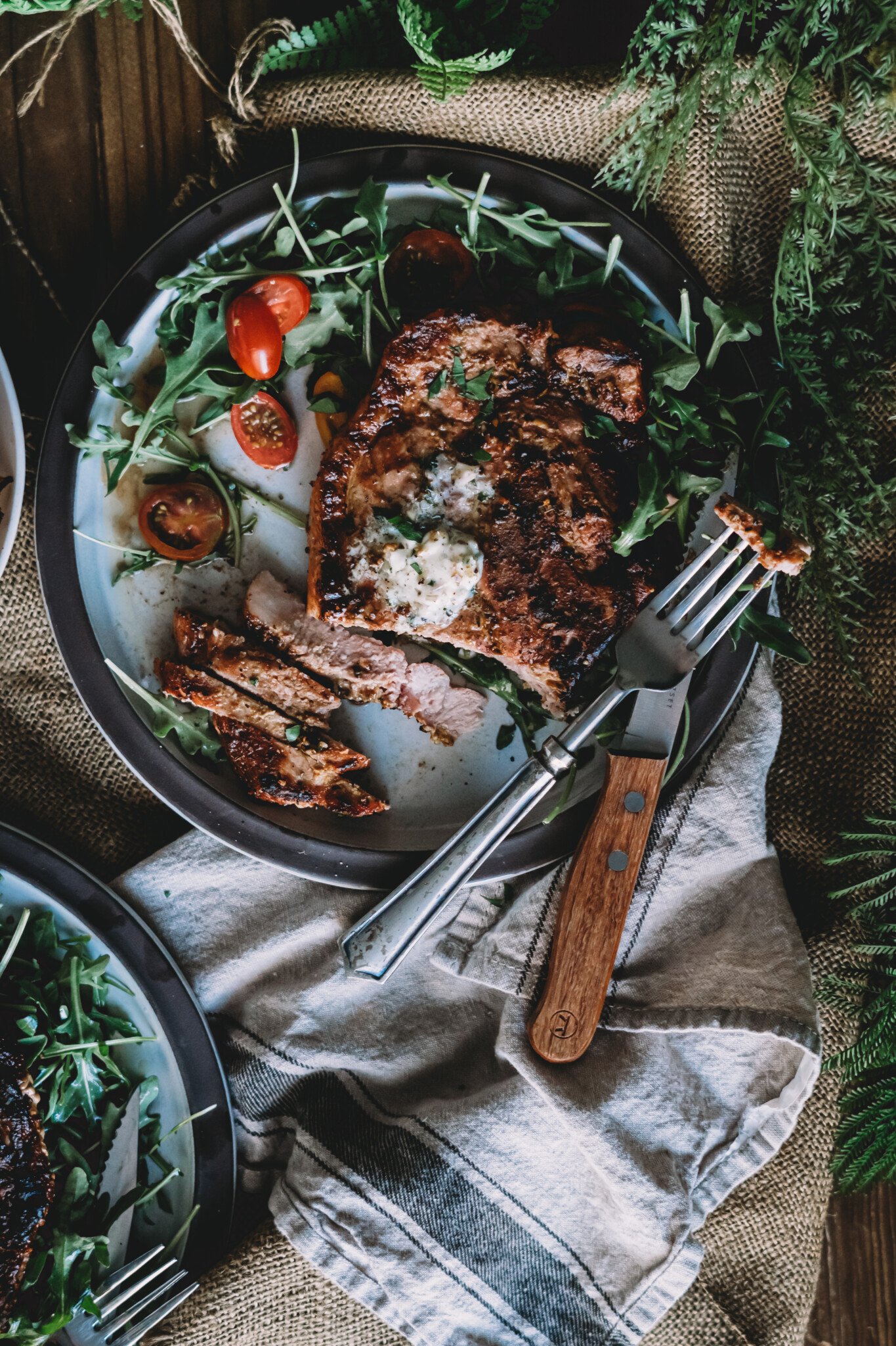 Knife and form slicing into pork chop on a plate with arugula and cherry tomatoes. 