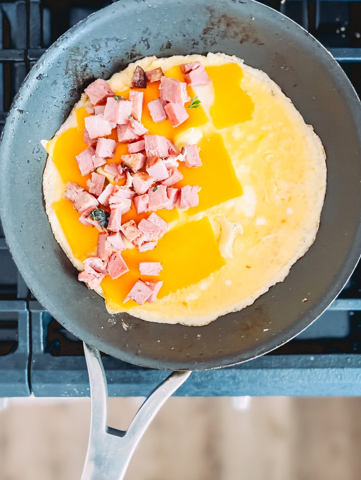 omelet being made in a skillet with cheese and ham on one side as egg sets.