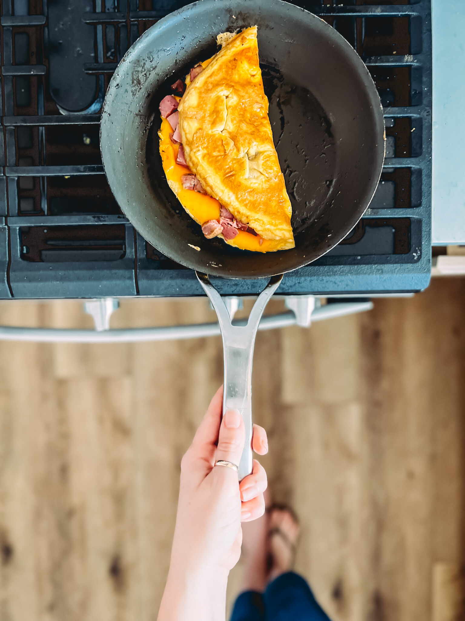 Ham and cheese omelet folded over in a skillet with hand holding handle. 