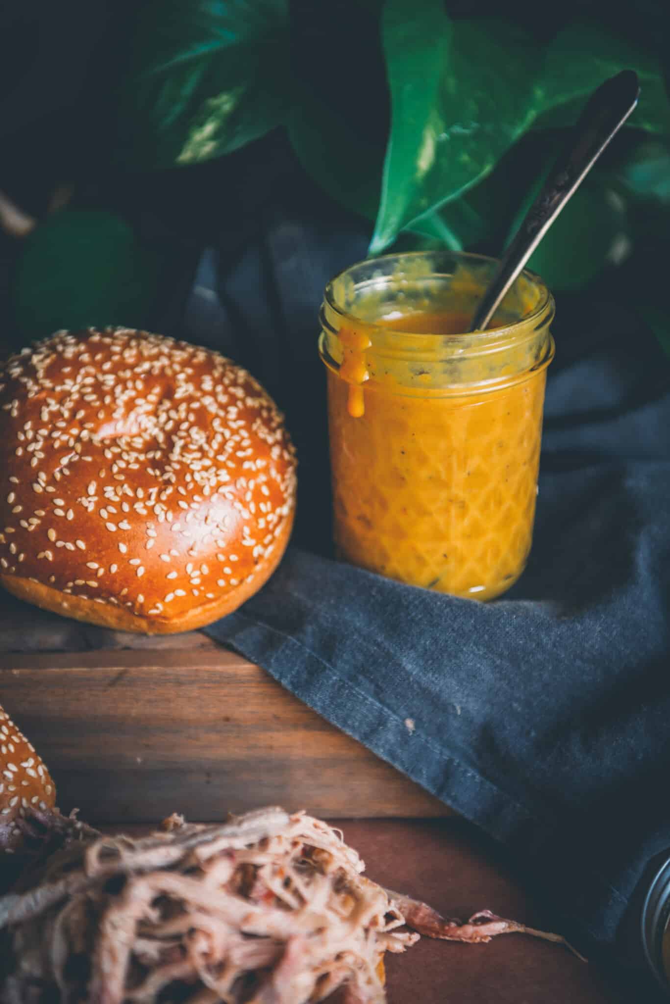 Msaon jar of bright yellow mustard barbecue sauce next to buns.