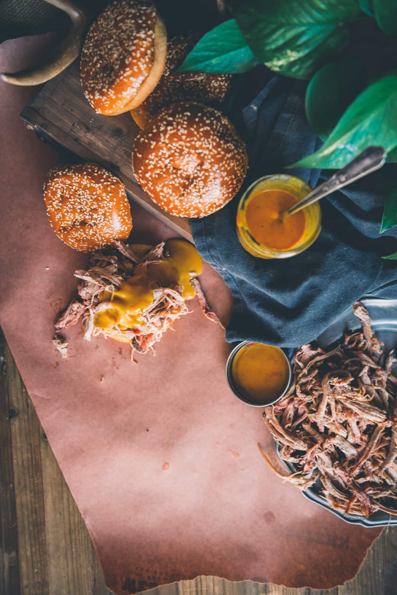 Overhead shot of yellow mustard sauce on pulled pork and in a jar, more pulled pork and buns near by. 