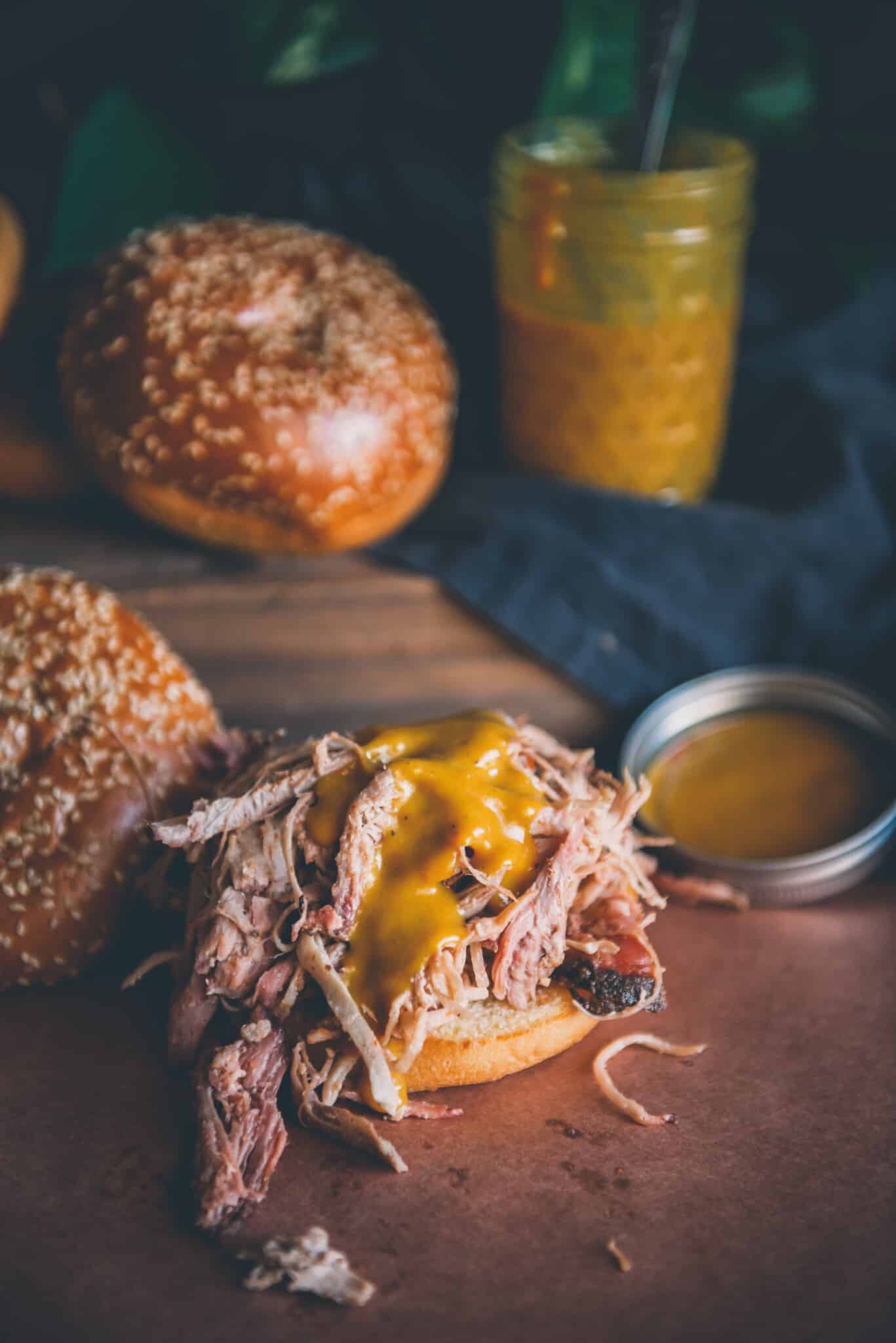 Close up of yellow mustard based sauce on a pile of shredded pork on a bun. 