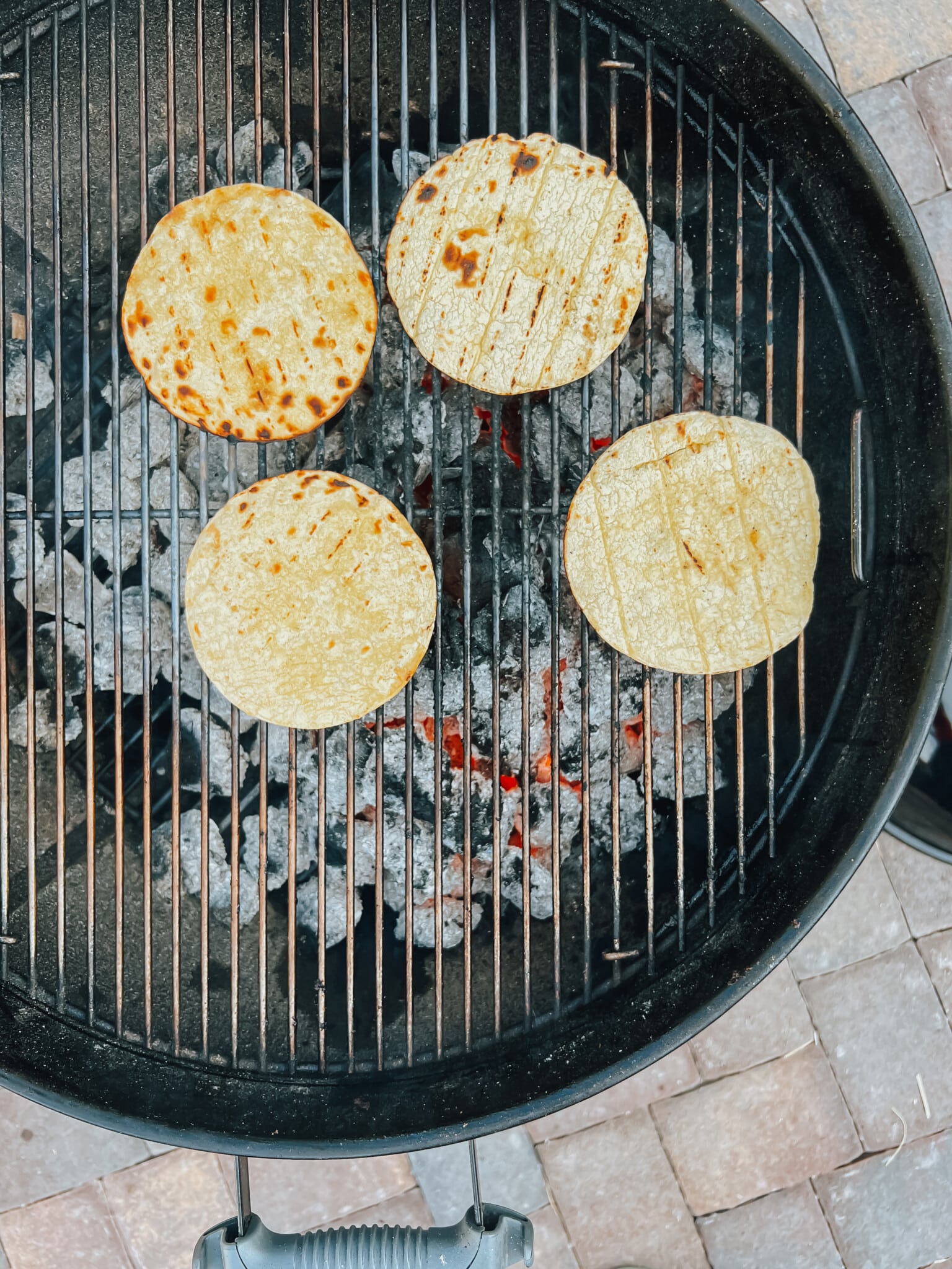 tortillas on grill grate over lit charcoal.