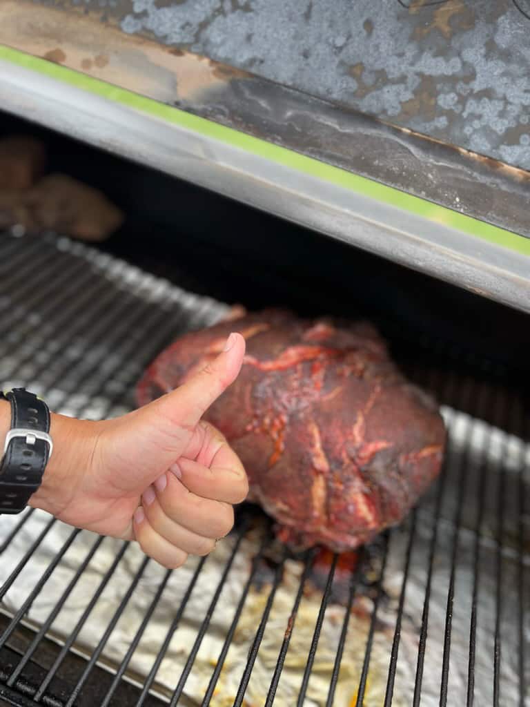 Hand with thumb up in front of smoking pork.