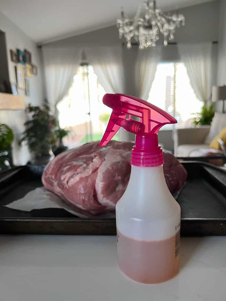 spray bottle of apple cider vinegar with pork butt in background