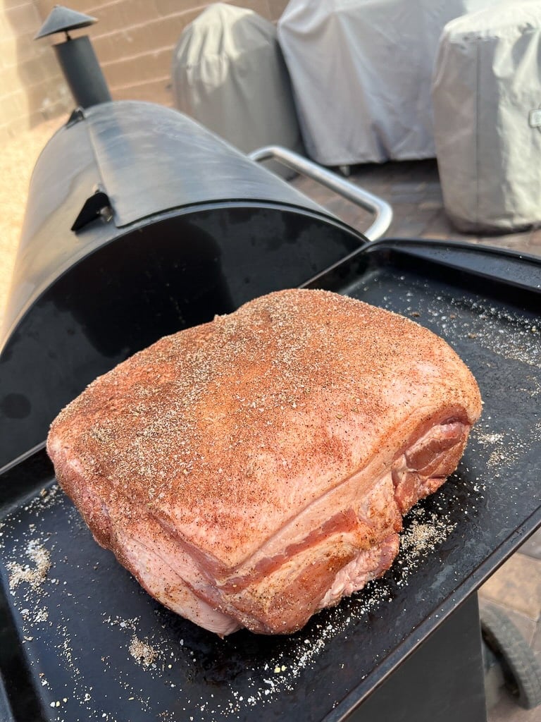 Pork shoulder rubbed in spices next to grill.
