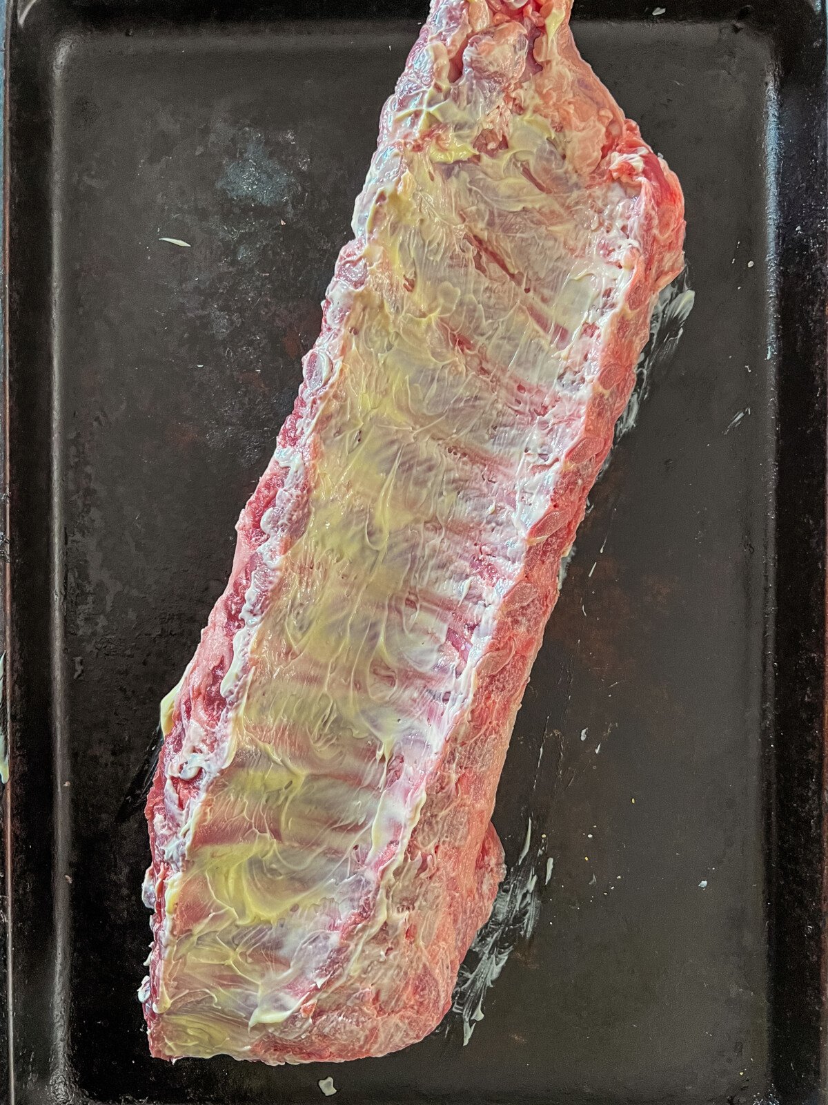 A rack of ribs, meat side down rubbed with mayo.
