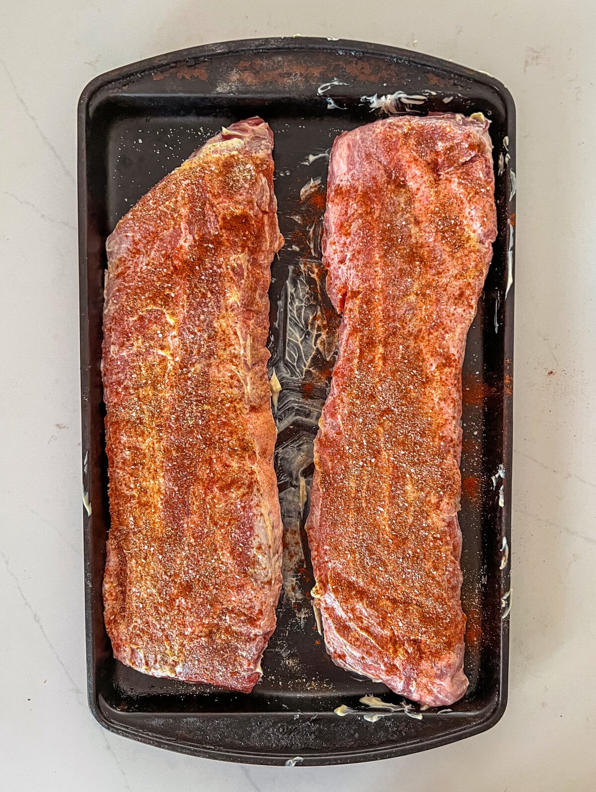 2 racks of baby back ribs rubbed with mayo and seasoned with spices.