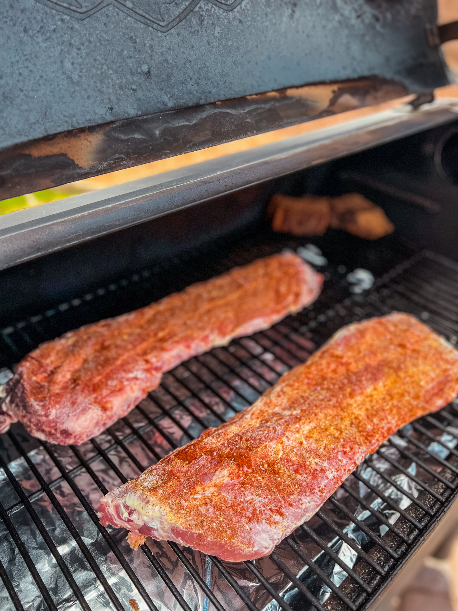 Raw baby back ribs rubbed with spices on grill grates.