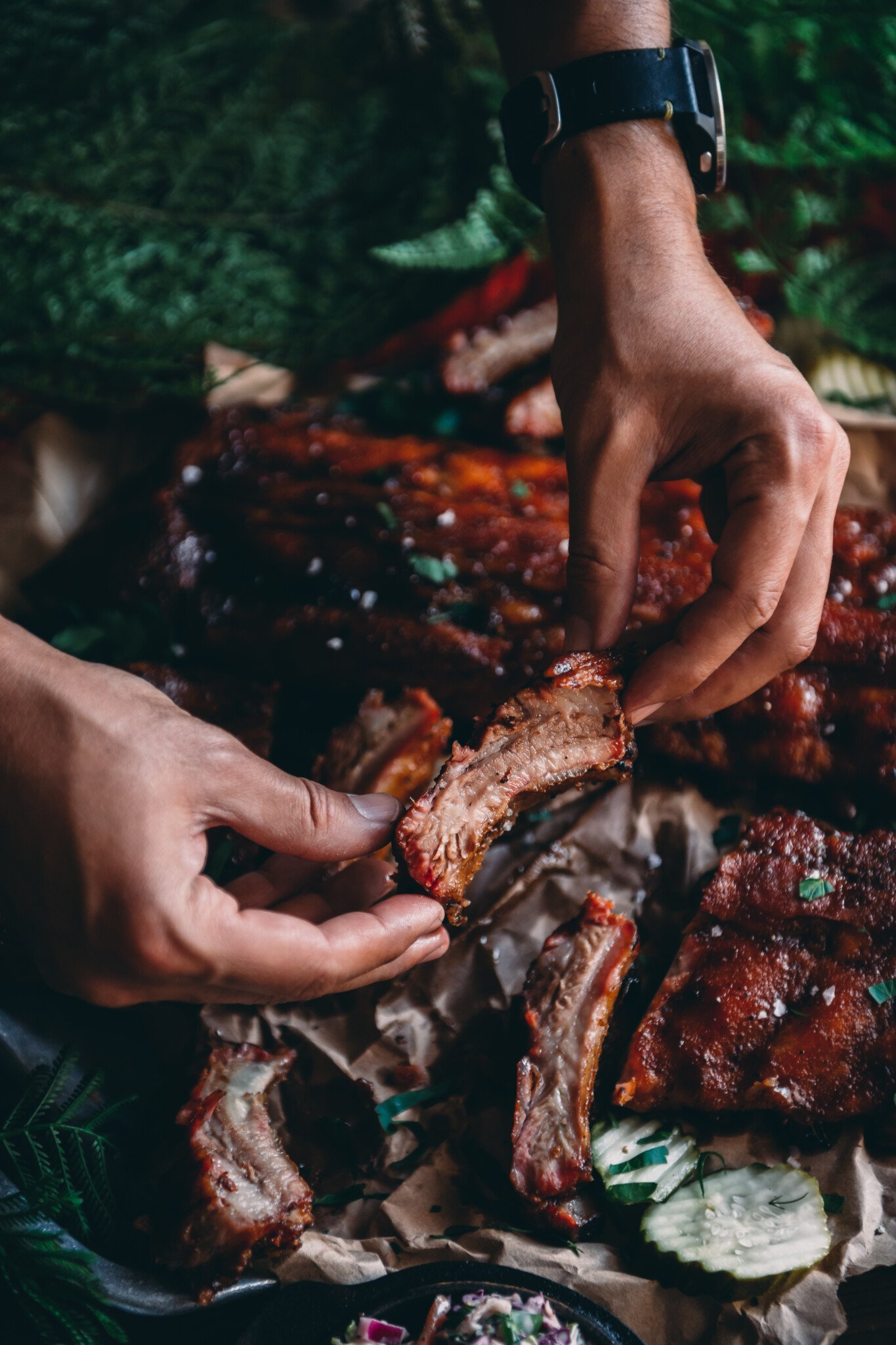 Hands picking up a smoked rib over a platter of them.