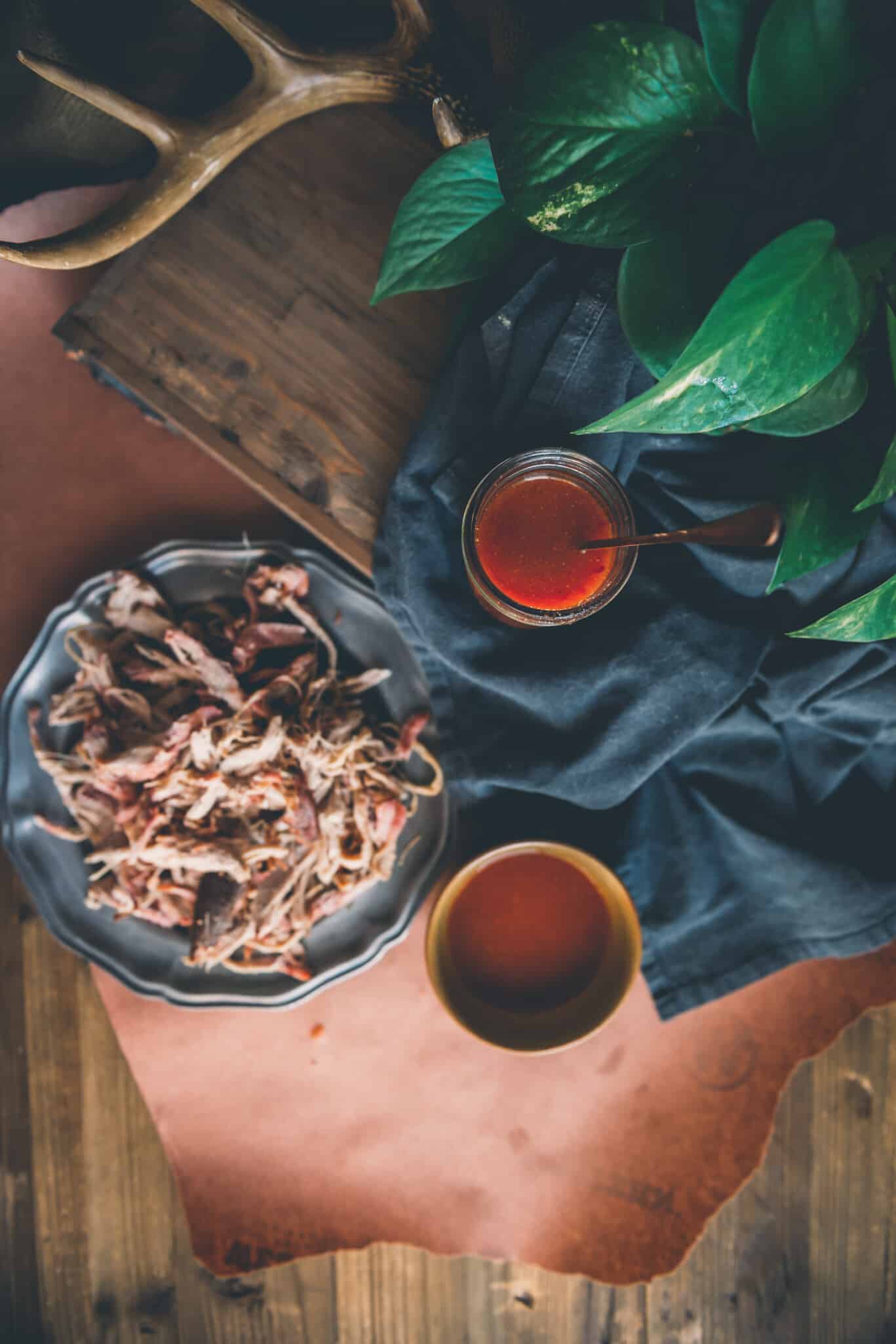 Overhead shot of jar of vinegar based bbq sauce, with another bowl of sauce along side a platter of shredded smoked pork. 