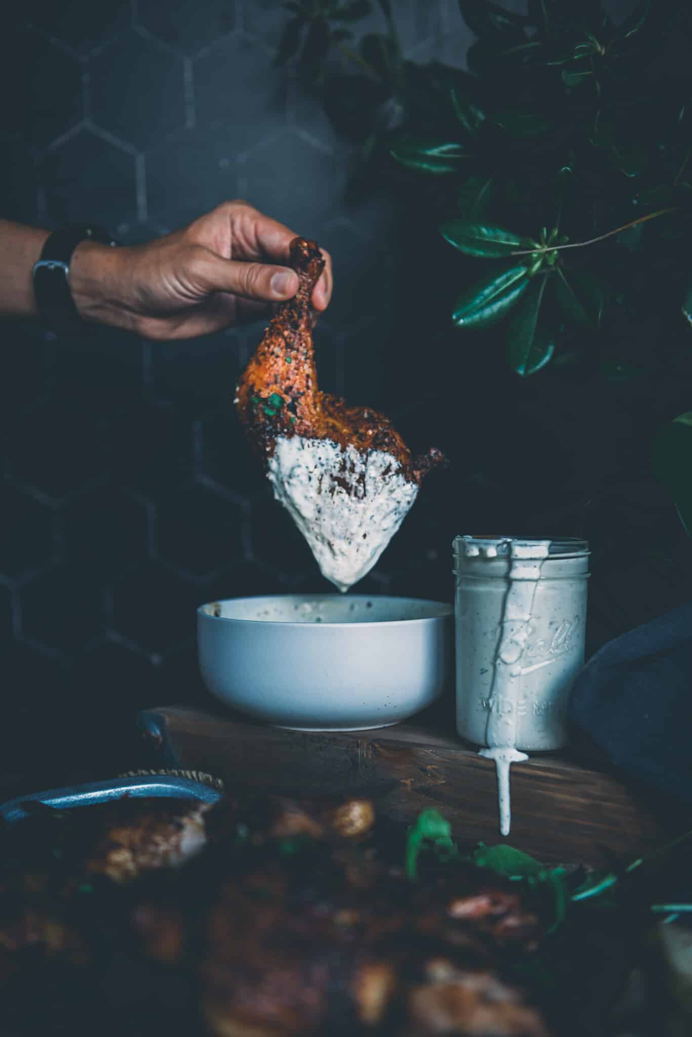 Hand dunking smoked chicken leg quarter into Alabama white bbq sauce. 