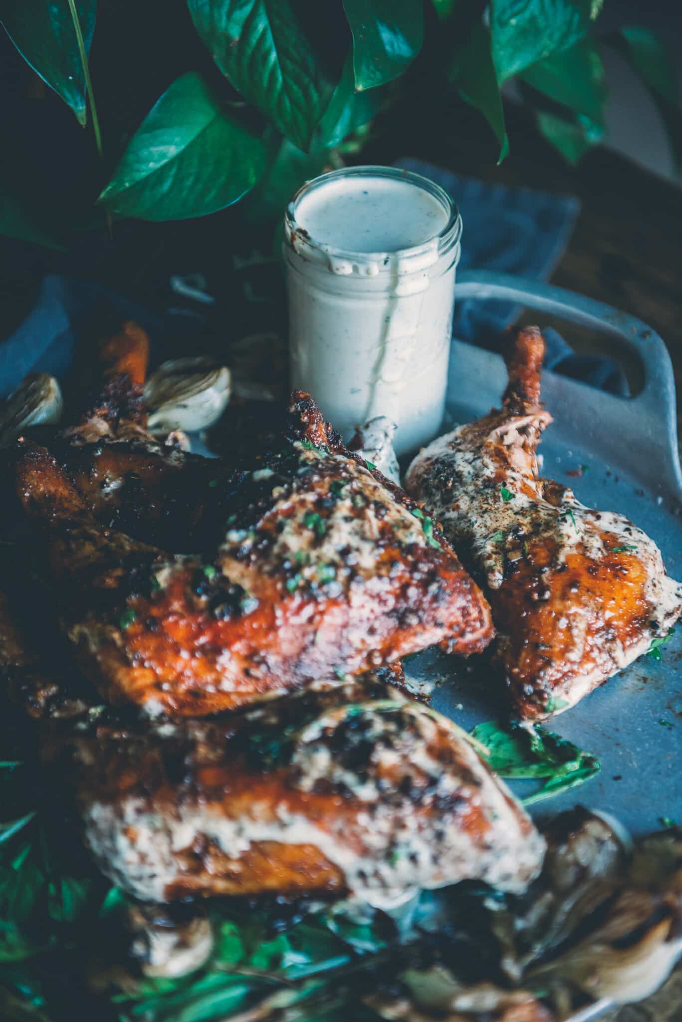 Jar of white bbq sauce on a platter with chicken slathered in it on a metal tray. 