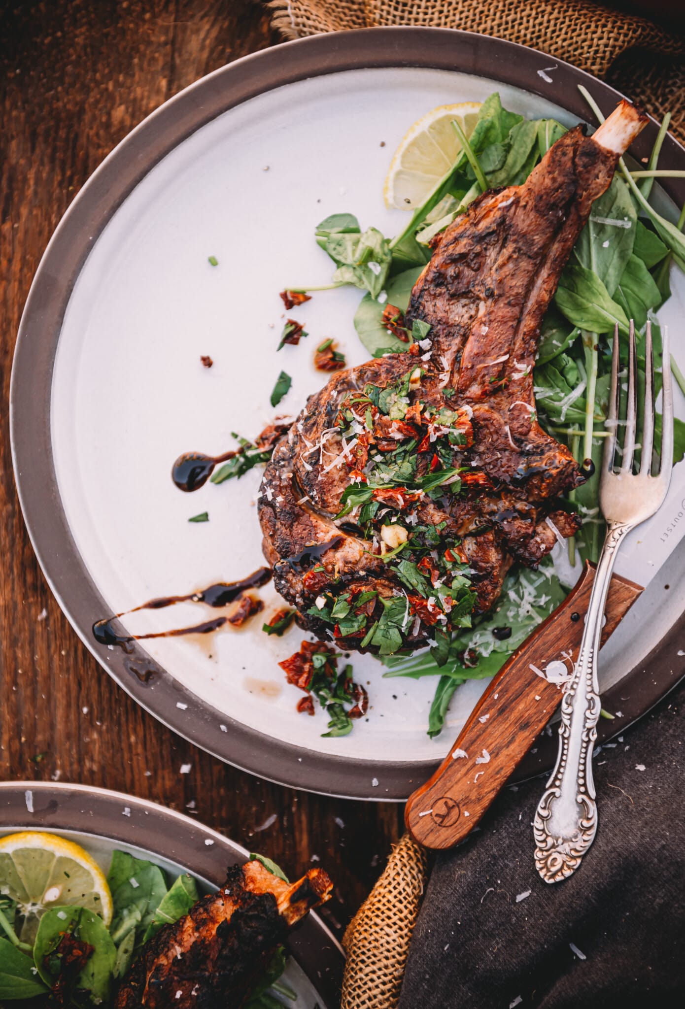 Single grilled veal chop on a white plate atop fresh arugula, topped with gremolata. 