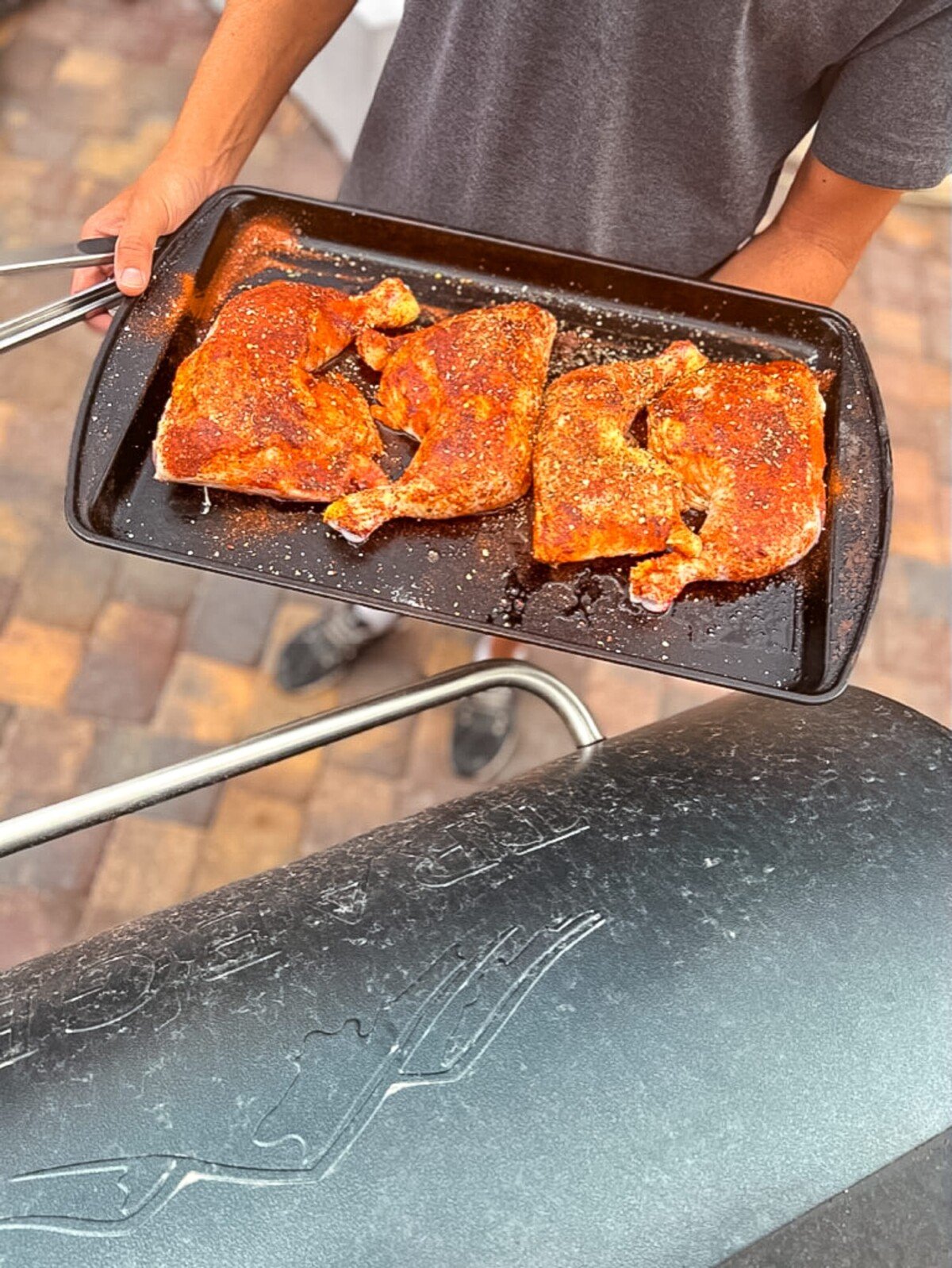 Hands holding platter of chicken legs before going on grill.