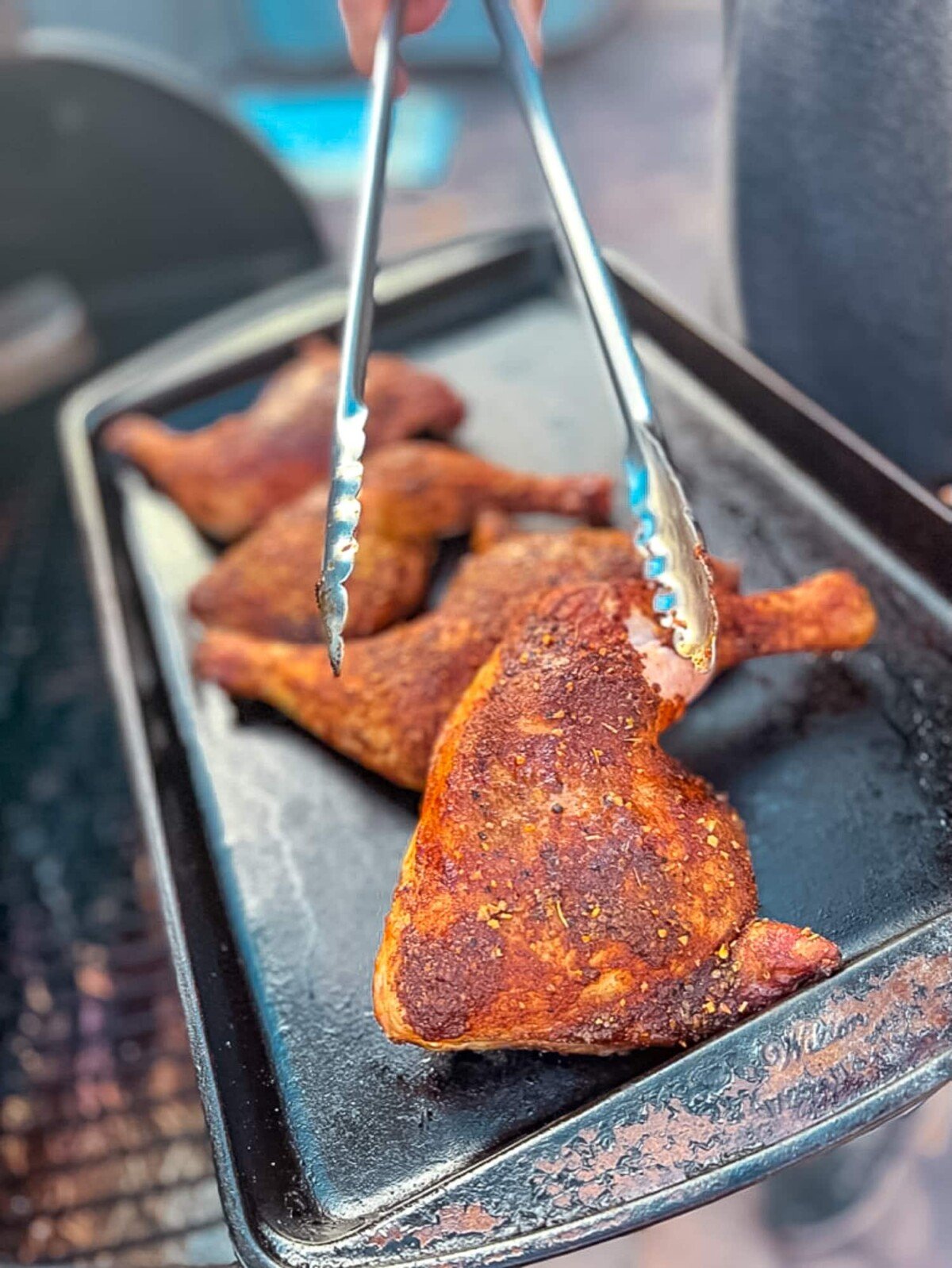 Smoked chicken quarters being placed on a baking sheet.