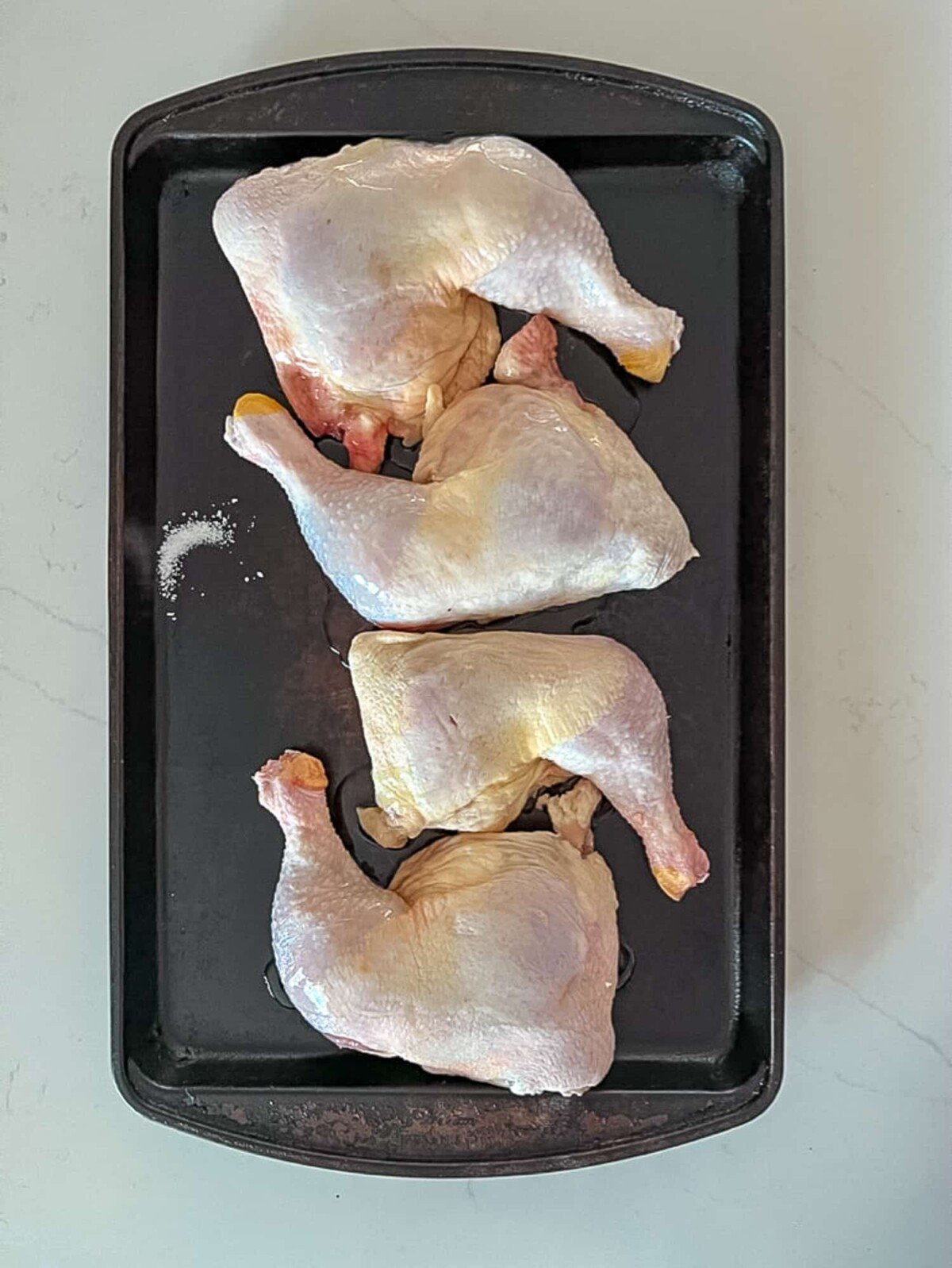 Raw chicken leg quarters on a baking sheet.