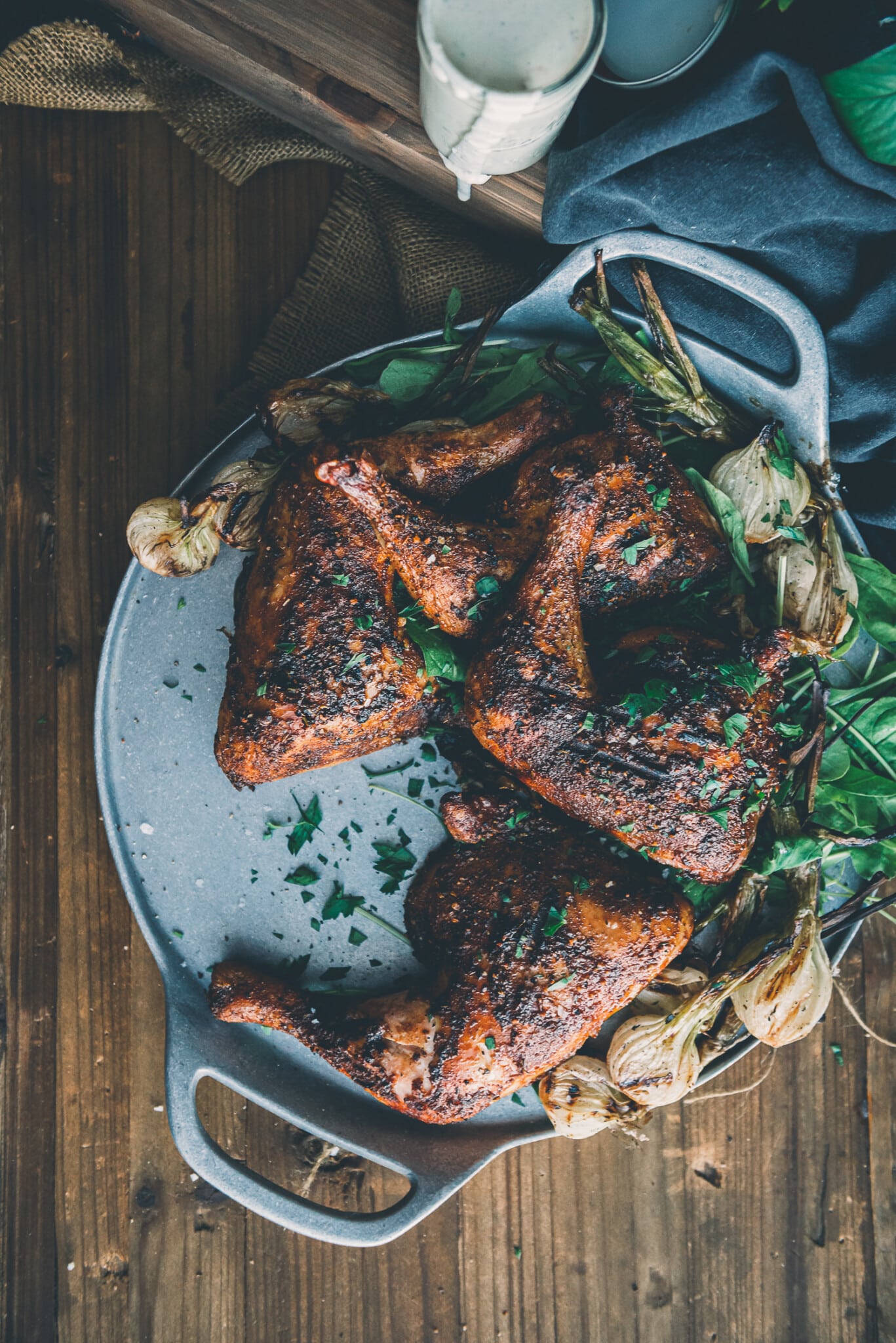 Above shot of a plate filled with smoked chicken quarters and grilled onions all garnished in chopped parsley. 