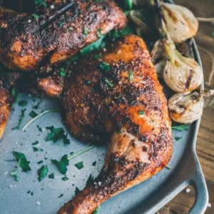 Chicken quarters on a serving platter with grilled spring onions; garnished in minced parsley.