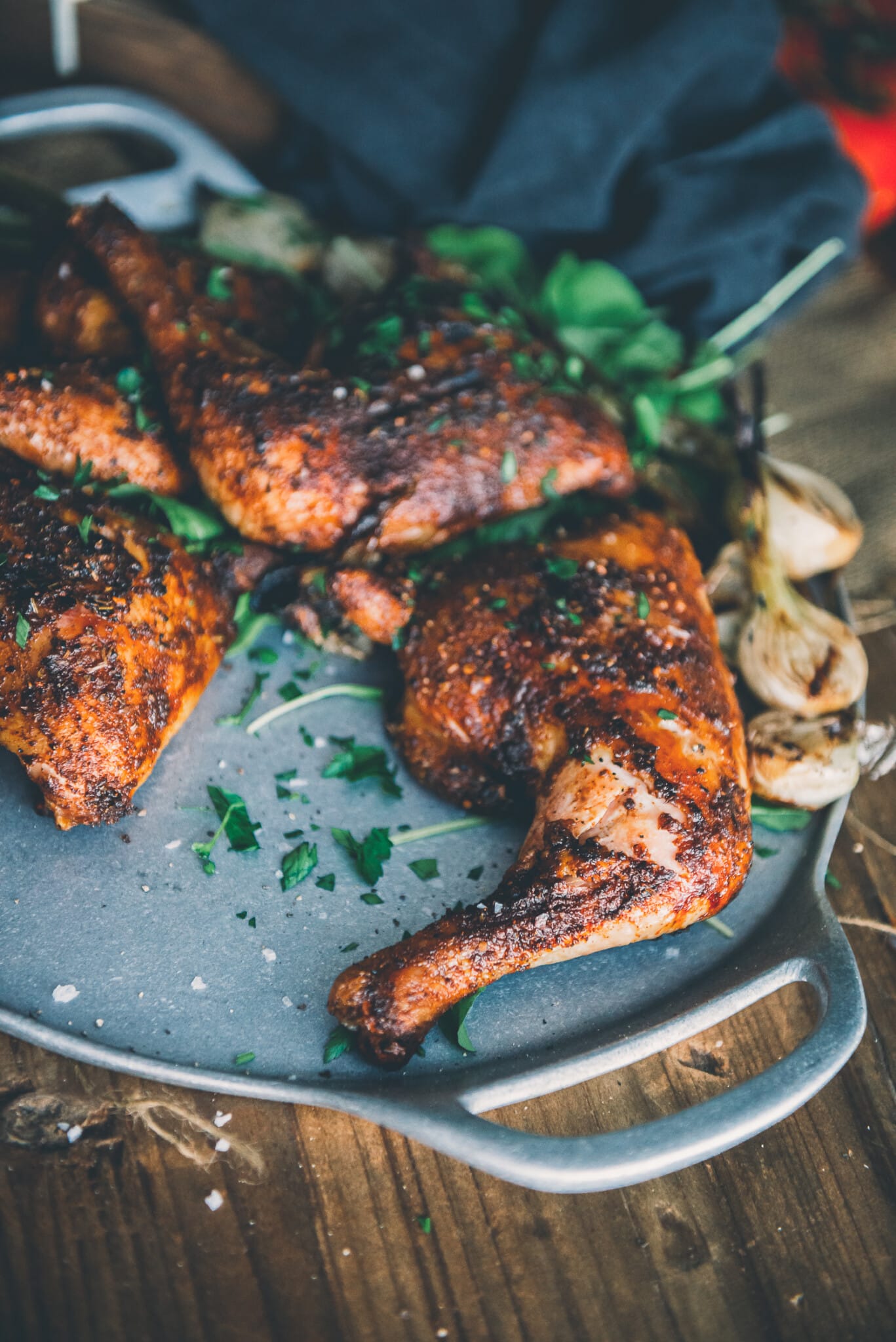 Platter of chicken quarters garnished with parsley and served alongside grilled spring onions. 