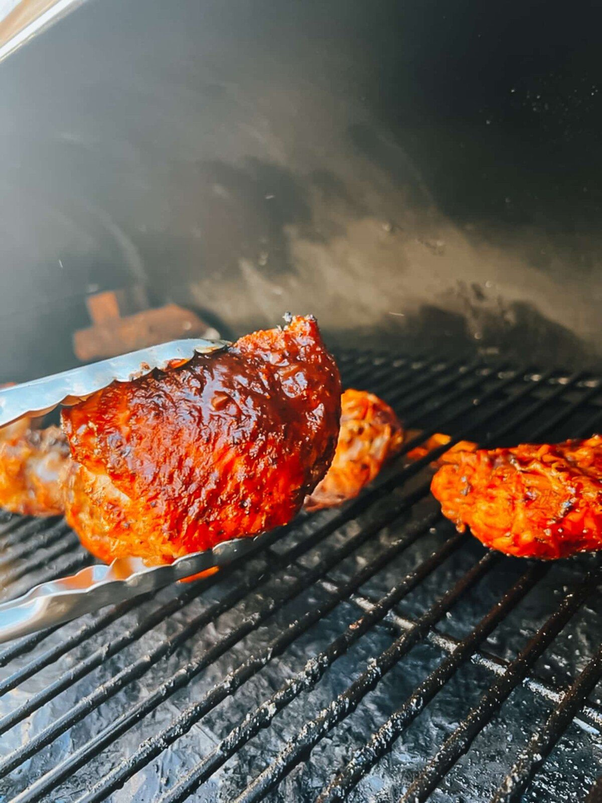 Thigh being held tong to show bbq chicken skin.