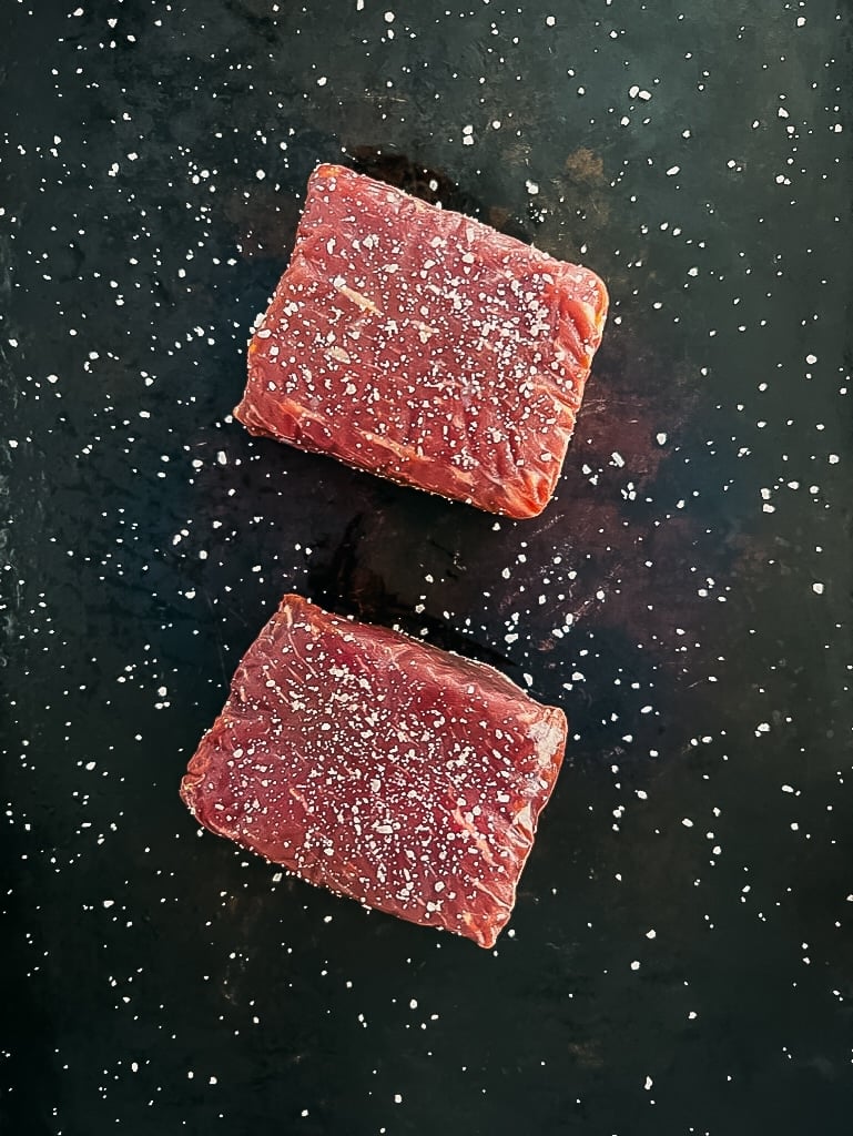 2 top sirloin steaks seasoned with salt on black background. 