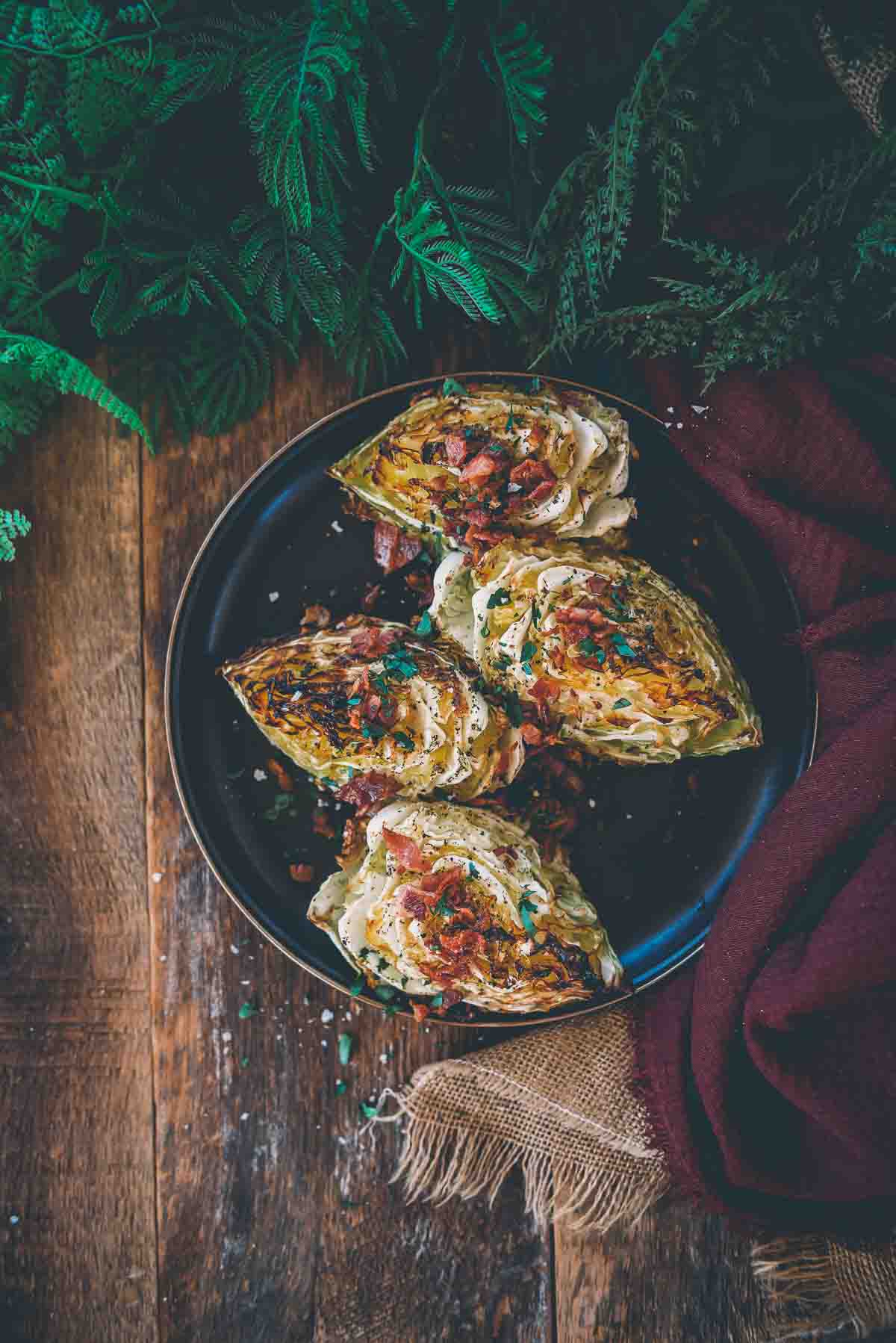 Above shot of smoked cabbage wedges lined up on a platter garnished with bacon and parsley. 