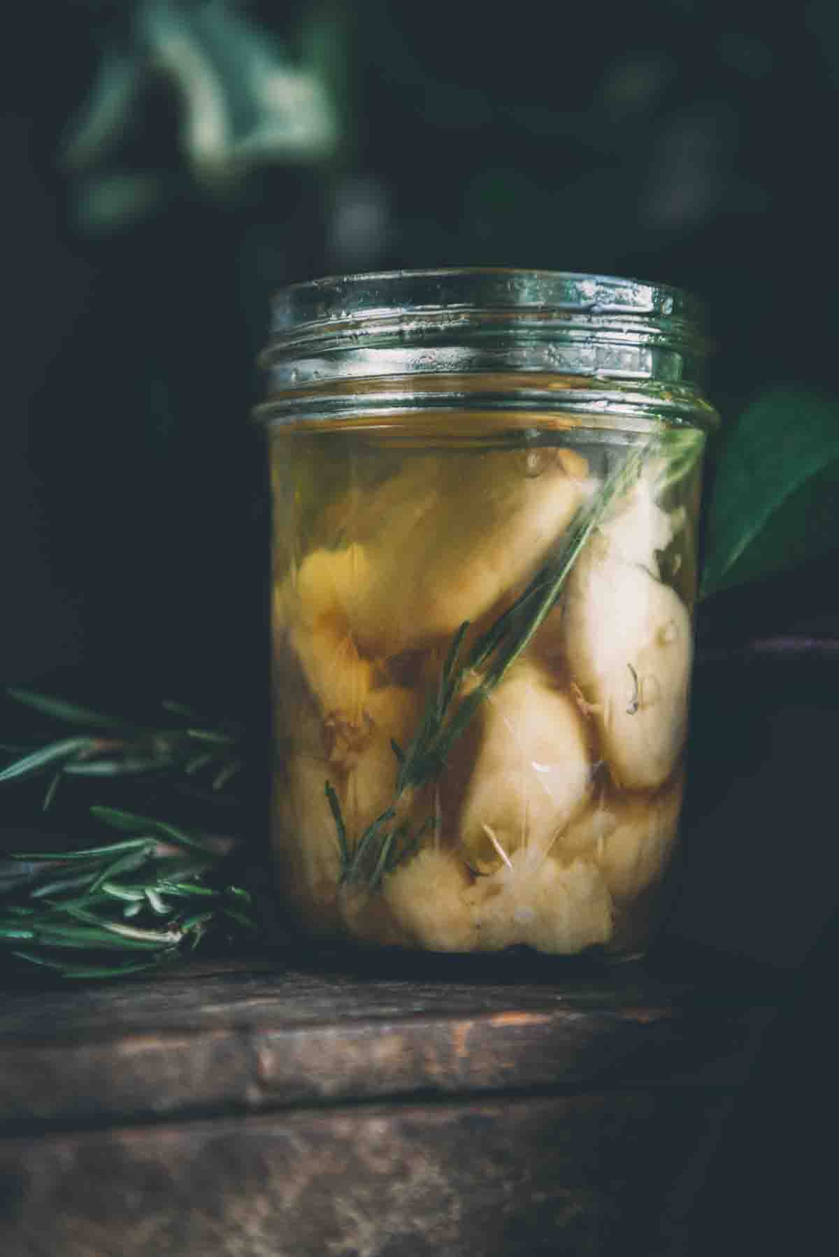 Side shot of mason jar to show smoked garlic confit and rosemary sprig.