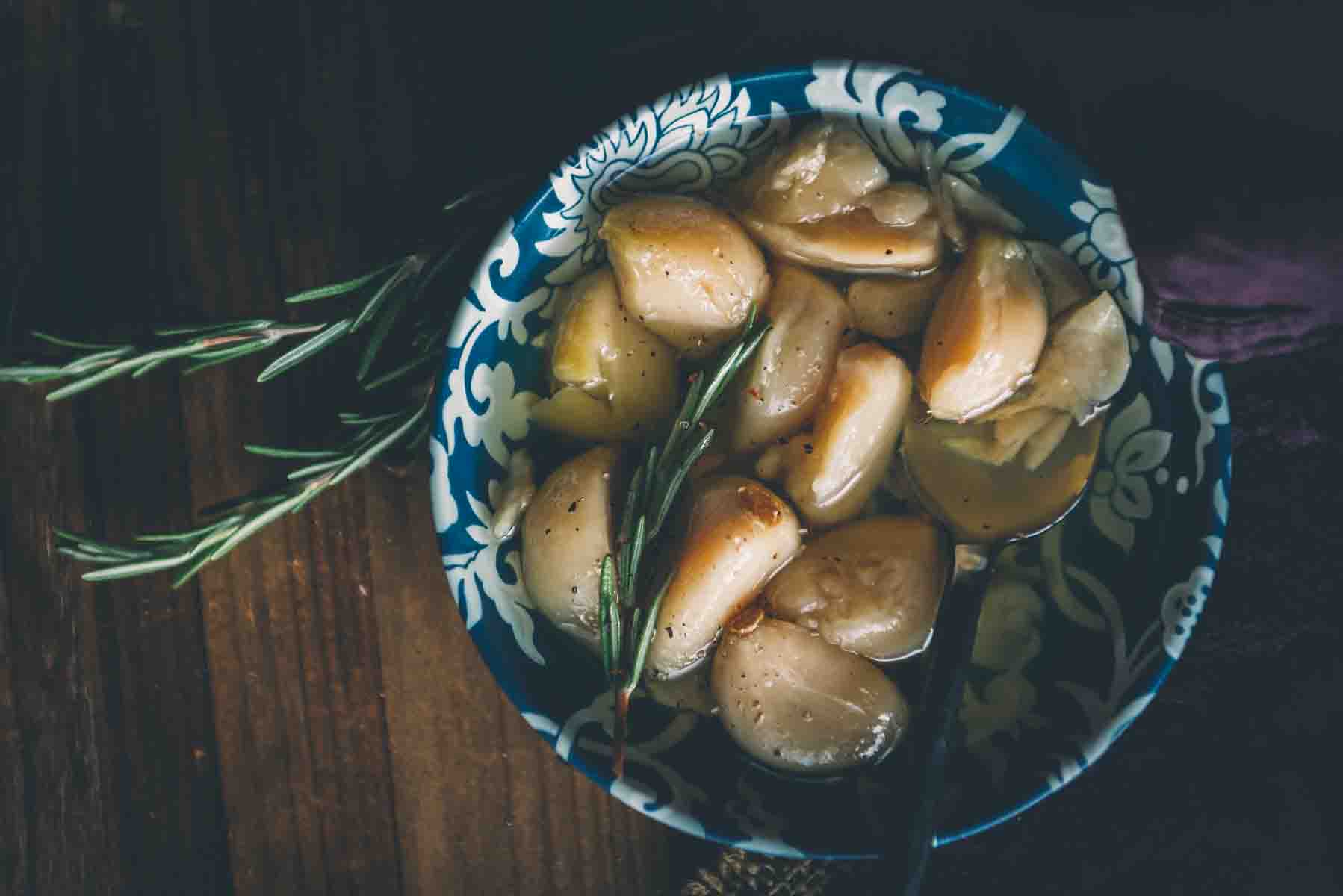 Above shot of smoked garlic confit in a blue bowl with rosemary and a spoon.