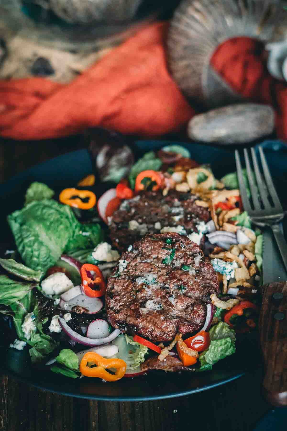 Smoked hamburgers over hearty steakhouse salad with sliced veggies and blue cheese crumbles. 