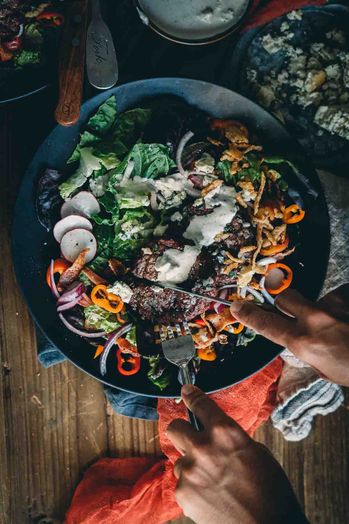 Overhead shots of hands slicing a burger over a salad with colorful vegetables. 
