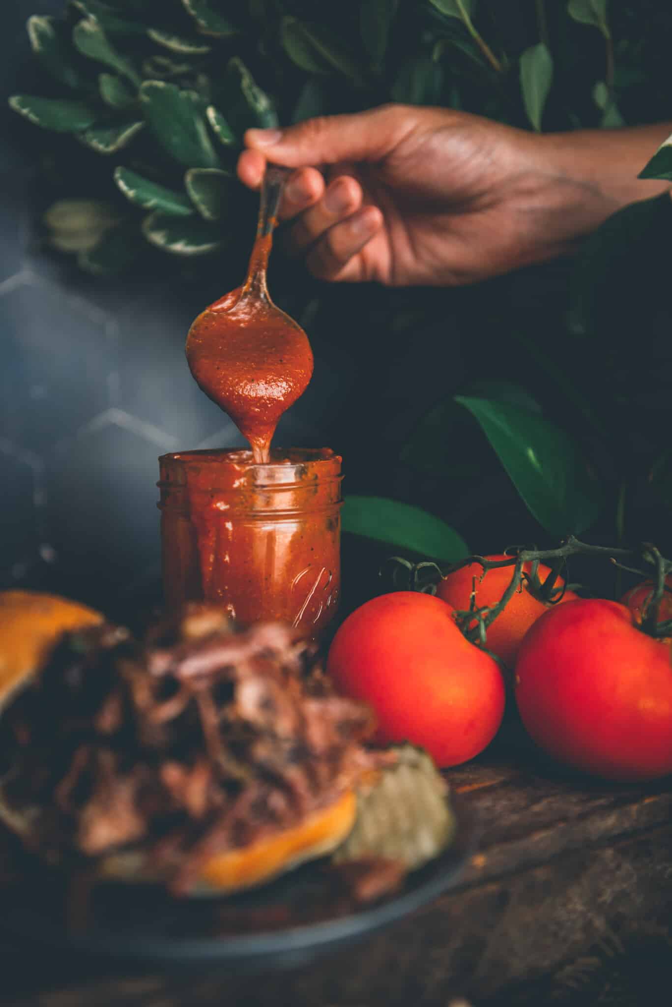 Hand pouring bbq sauce from a spoon into a jar. 