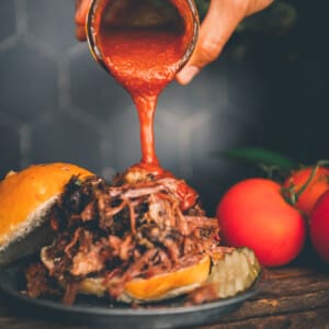 A person drizzling Keto BBQ Sauce on a bbq burger.