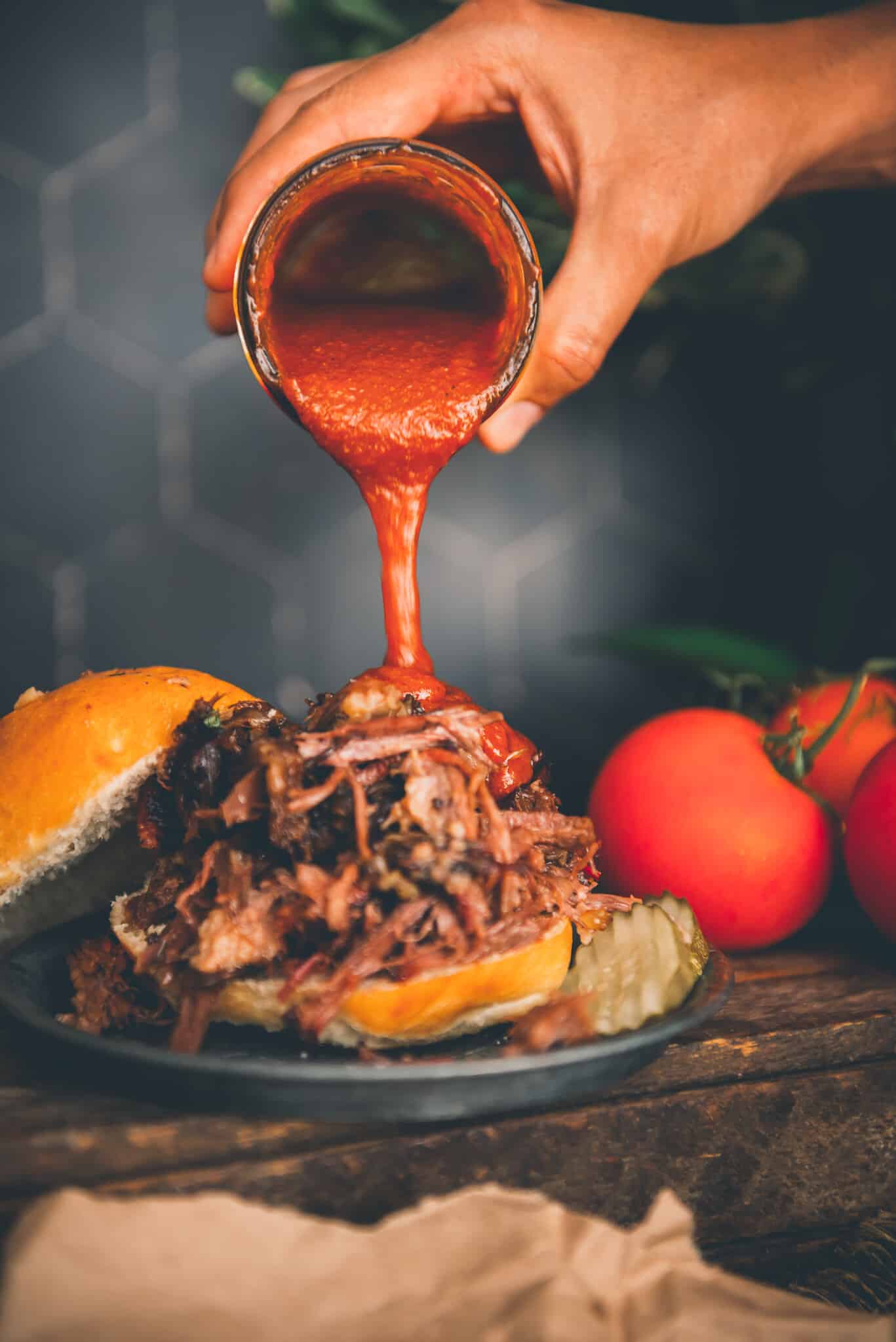 Hand pouring homemade keto bbq sauce over shredded beef sandwich. 